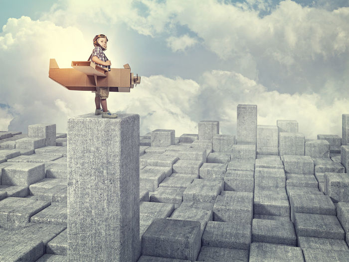 Digital composite image of boy with wings standing on concrete block against sky