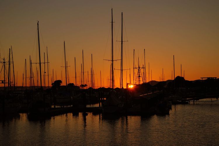Silhouette boats moored at harbor during sunset