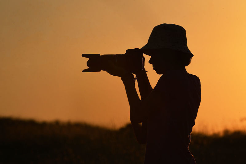 Young photographer photographing through digital camera silhouette against sunset