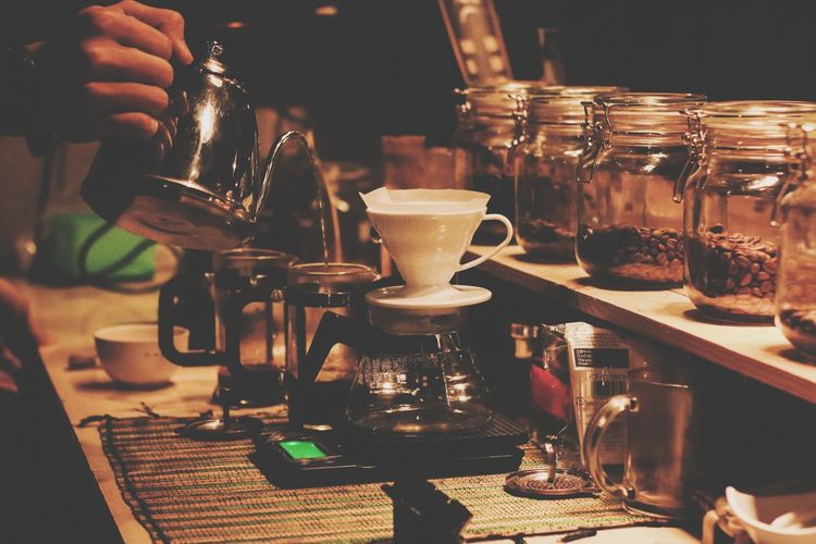 Cropped hand of barista pouring water in container at coffee shop