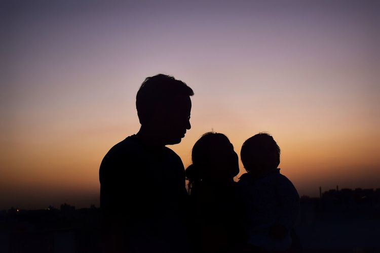 Silhouette family against orange sky during sunset
