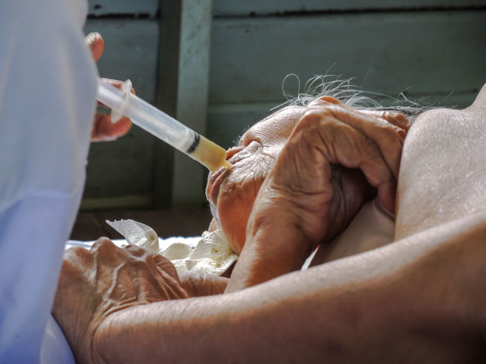 Midsection of doctor feeding senior woman through syringe 