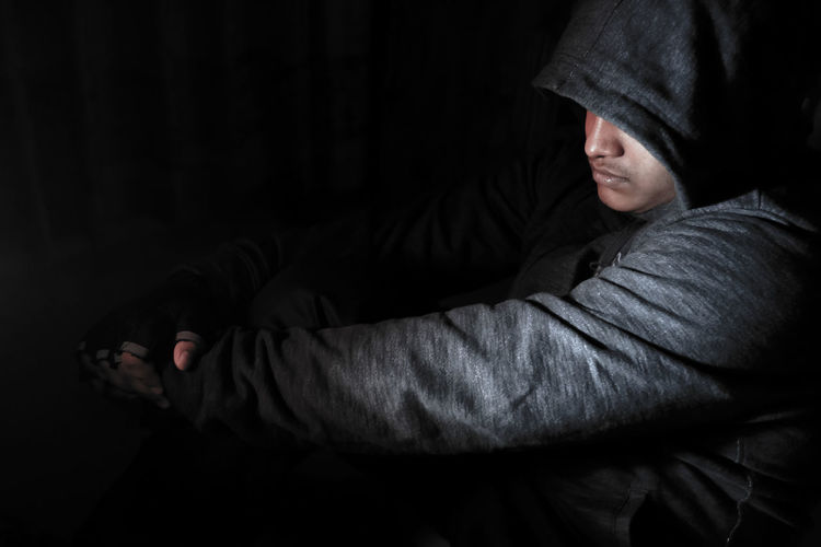 Hooded depressed man sitting on floor in dark room.