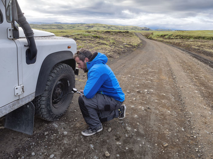 Man kneeling while examining tire pressure through equipment at roadside