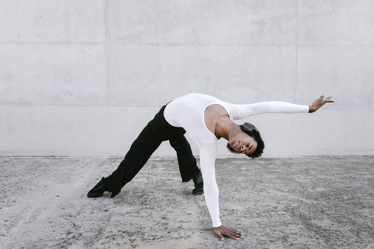 Flexible man bending over backwards while dancing against white wall