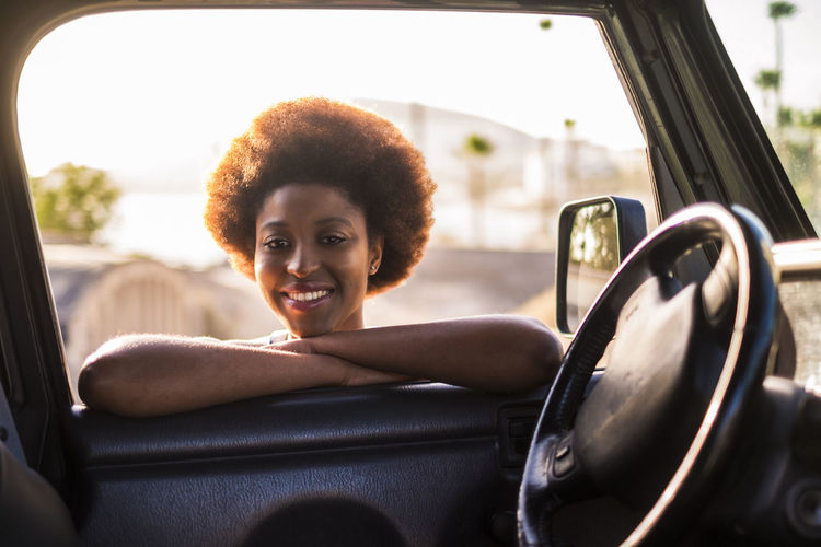 Portrait of smiling young woman leaning on car window