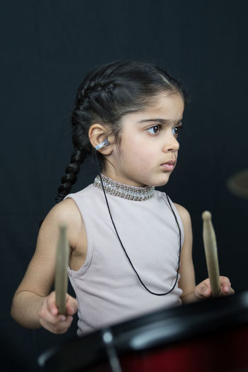 Girl playing drum while standing against curtain