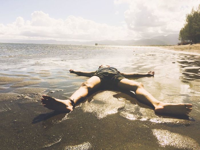 Full length of shirtless man lying at beach against sky