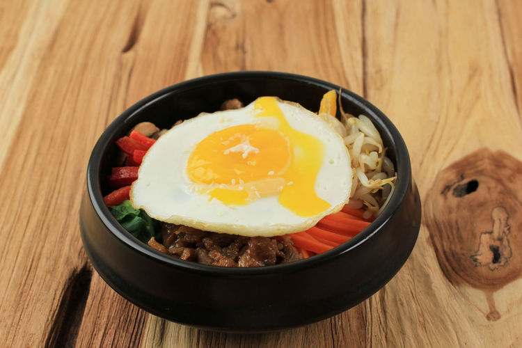 Bibimbap with sunny side egg on a wooden background, traditional korean mixed rice dish