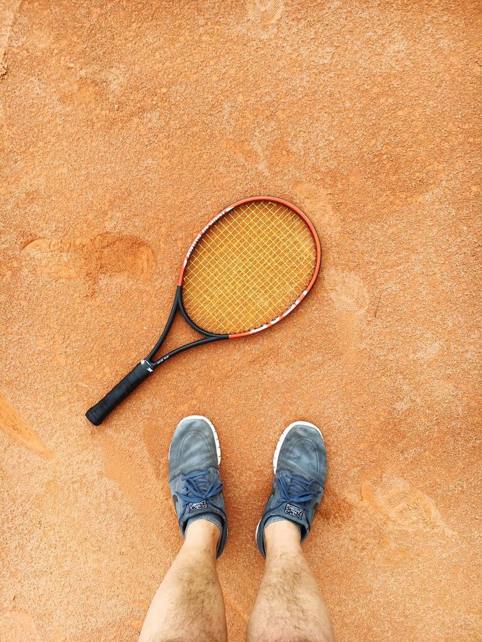 Low section of man standing by tennis racket on clay court
