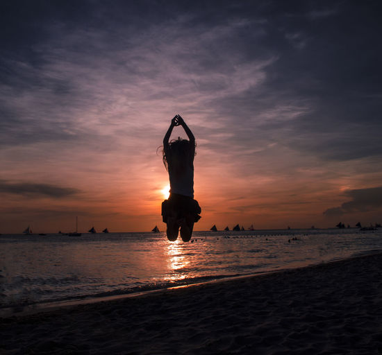 Silhouette woman jumping at beach against cloudy sky during sunset