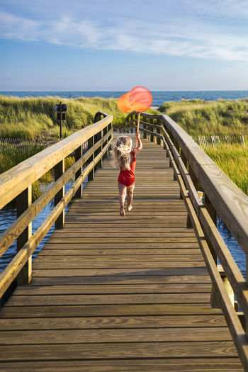 Little girl from behind running on bridge to beach with red fishingnet