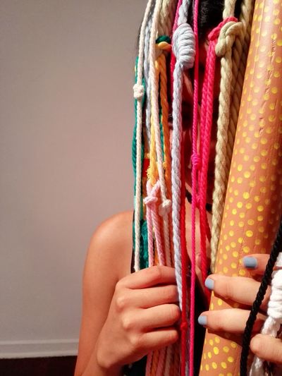 Close-up of woman hiding behind colorful strings against wall