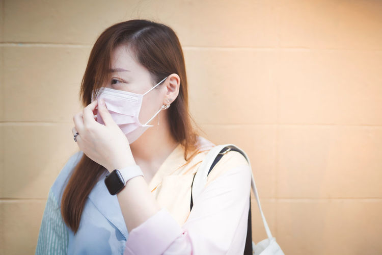 Portrait of a young woman against wall with face mask