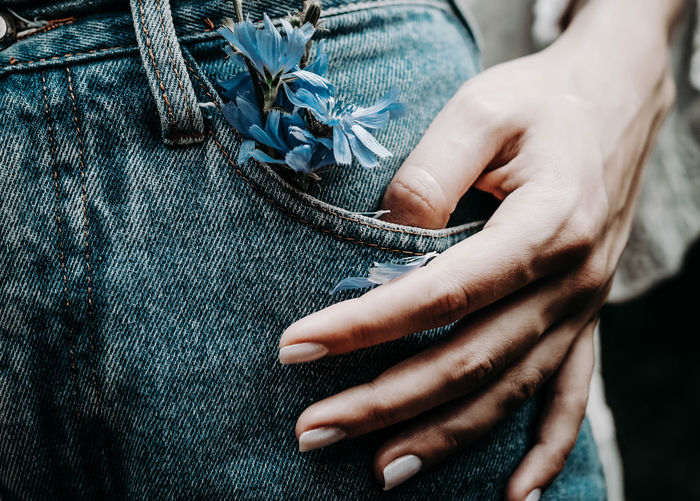 Close-up of a female hand in a jeans pocket with blue wildflowers