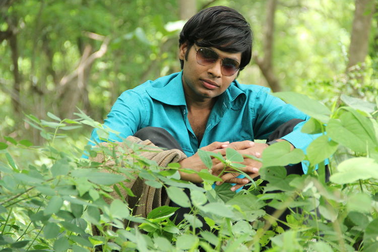 Portrait of young man holding plant in forest