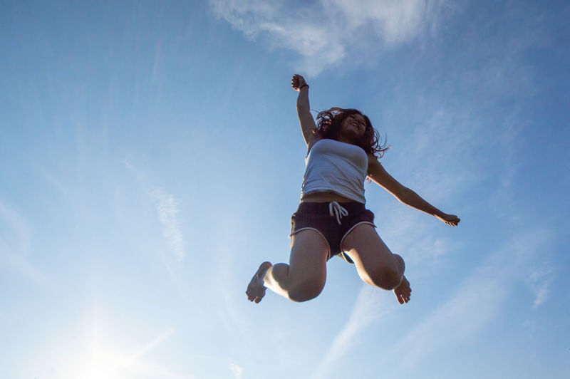 Low angle view of teenage girl jumping against blue sky
