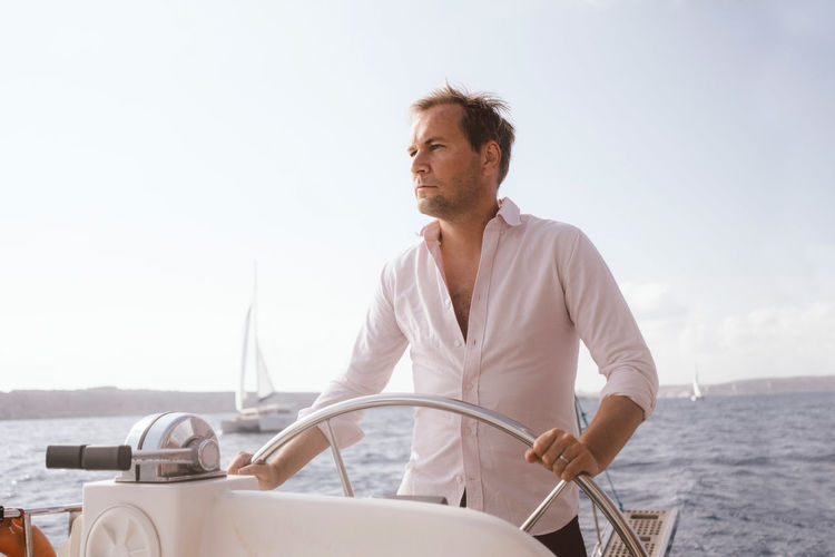 Confident mature man sailing catamaran with helm on sea against sky