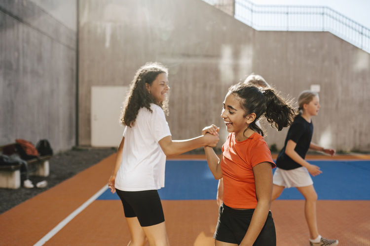 Happy female friends holding hands while playing in basketball court