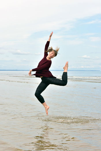 Mid adult woman jumping on shore against sky