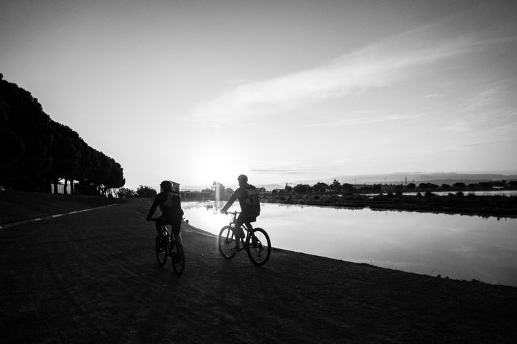 Silhouette people riding bicycle on water against sky
