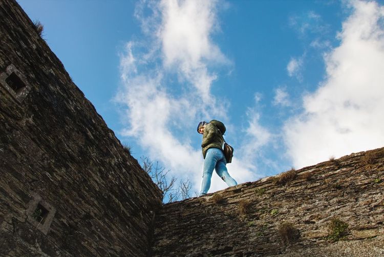 Low angle view of woman walking on surrounding wall against cloudy sky