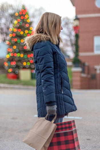 Side view of woman holding shopping bags while standing on road