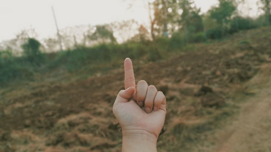 Cropped hand of person gesturing against hill