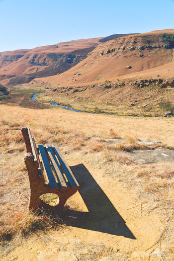 Empty bench on field by mountain against sky