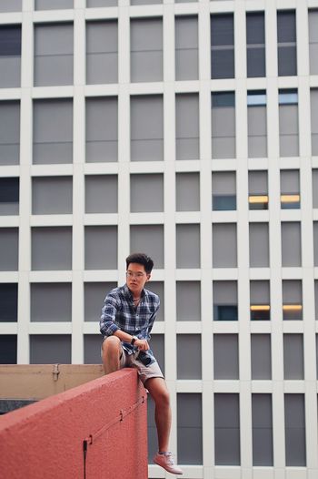 Young man with camera sitting on railing against building