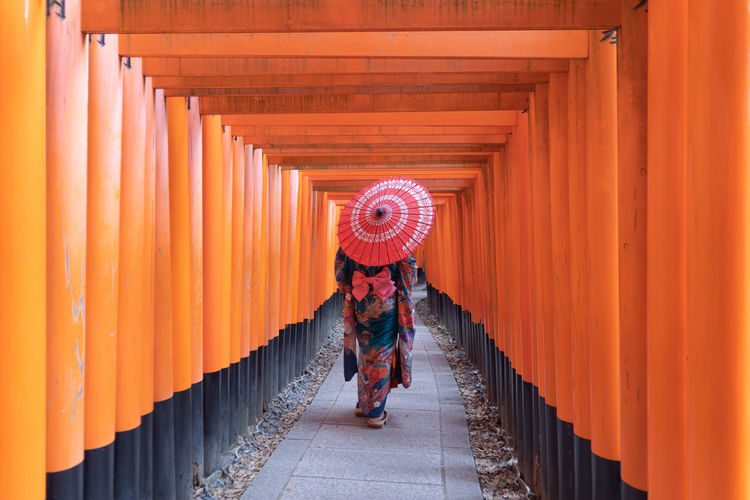 Full length rear view of woman with umbrella walking in corridor