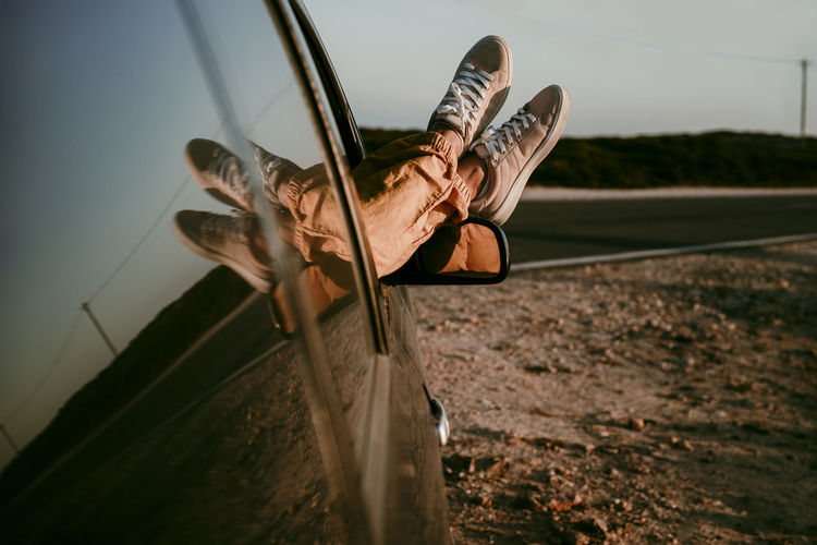Woman relaxing legs on car window during sunset