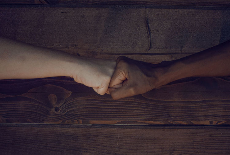 Fist bump of two women black and caucasian on a wooden background