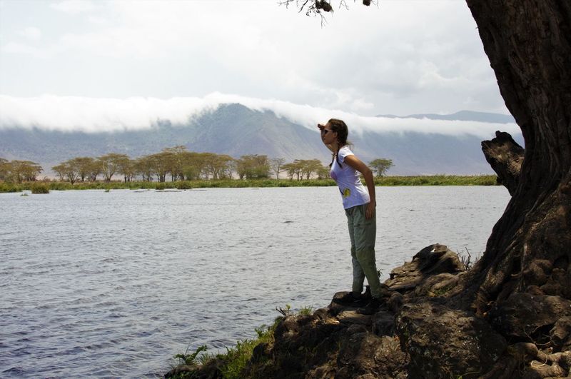 Side view of woman shielding eyes while standing at lakeshore in ngorongoro conservation area