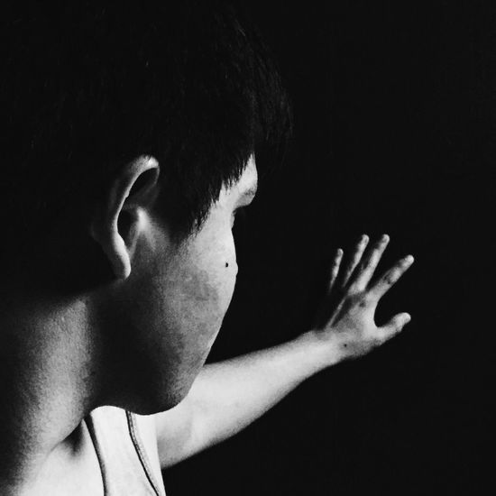 Close-up of young man showing stop gesture against black background