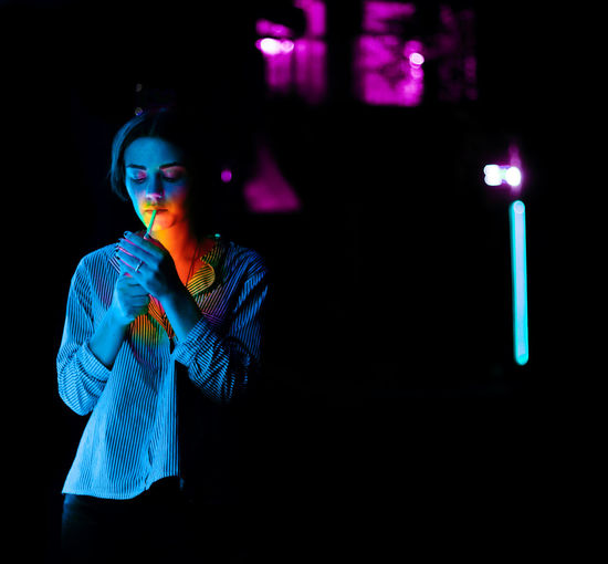 Portrait of young woman standing against illuminated street at night