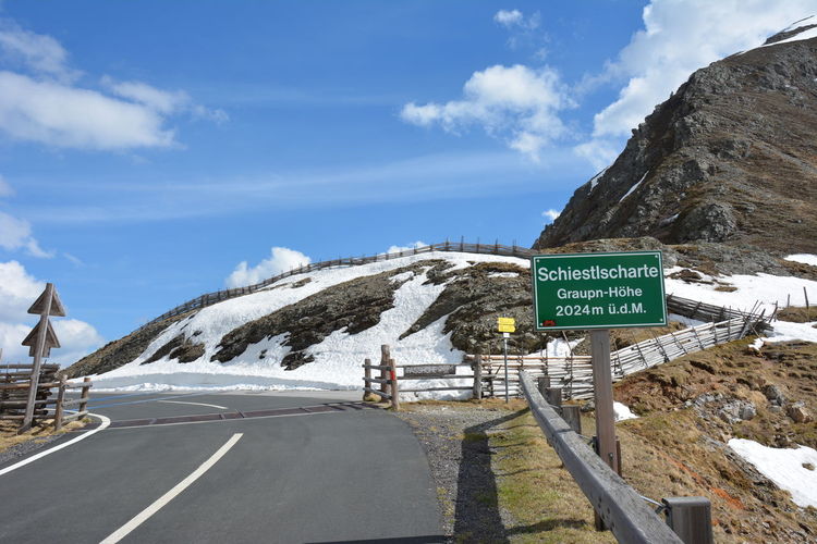 Road sign by snowcapped mountain against sky