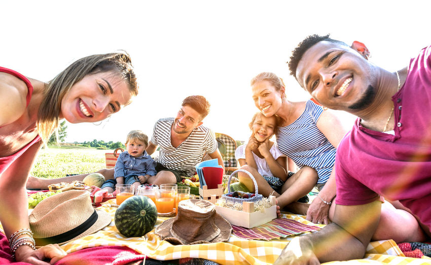 Portrait of happy family and friends sitting on field during picnic