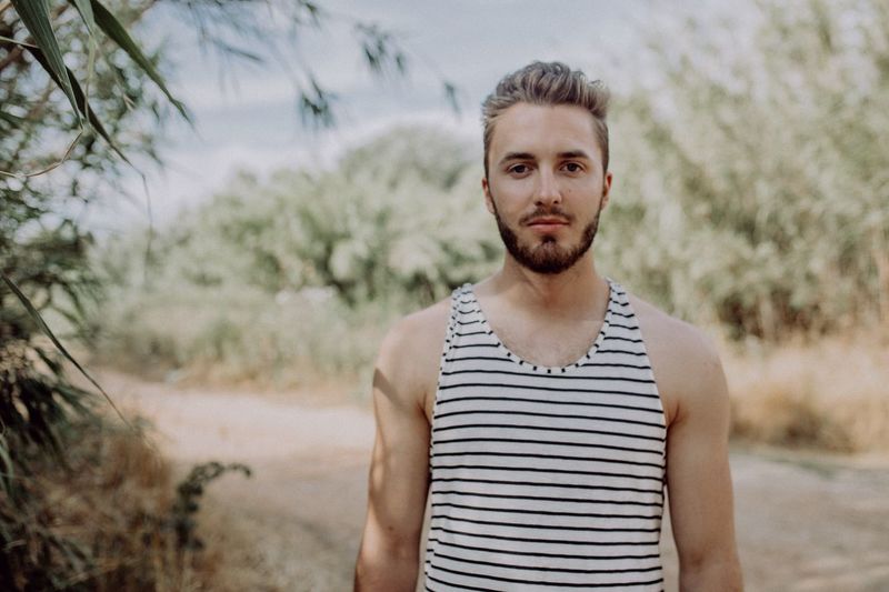 Portrait of handsome man wearing striped tank top while standing on field