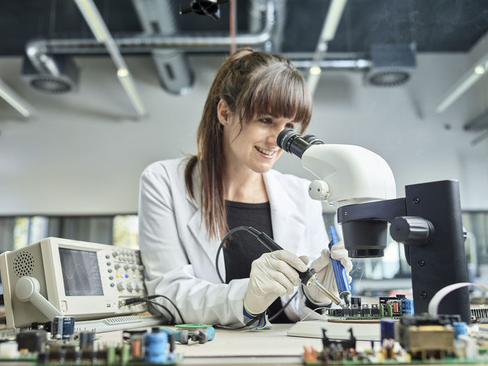 Female technician soldering under microscope