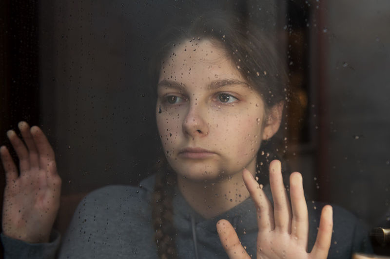 Young girl is looking with hope the window on which raindrops, autumn mood, loneliness