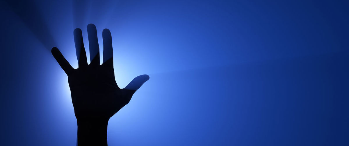 Low angle view of silhouette hand against blue sky