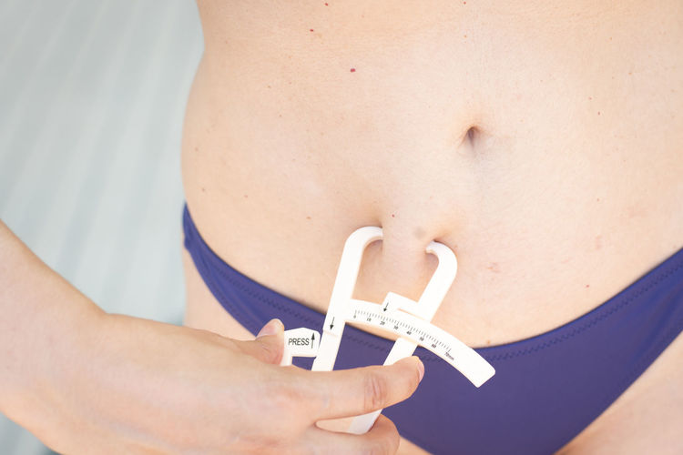 Midsection of woman checking belly fat with caliper