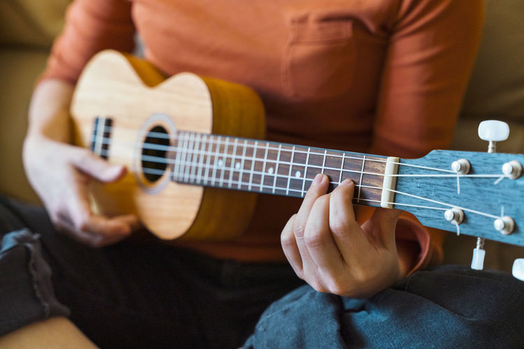 Midsection of woman playing ukulele at home
