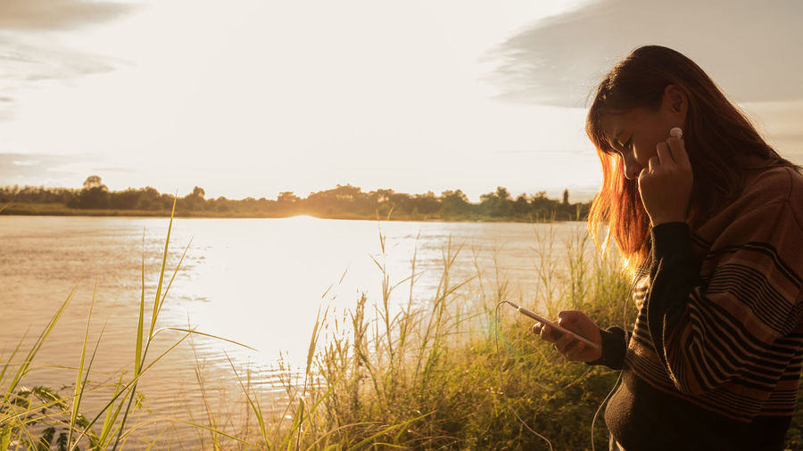 Rear view of woman photographing by lake against sky
