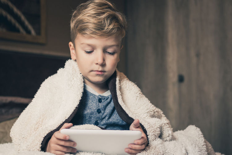 Boy using digital tablet while sitting against wall at home