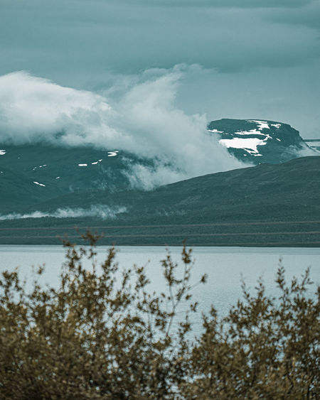 Scenic view of sea by snowcapped mountains against sky
