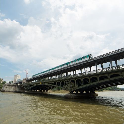 Low angle view of train moving on pont de bir-hakeim over seine river against cloudy sky