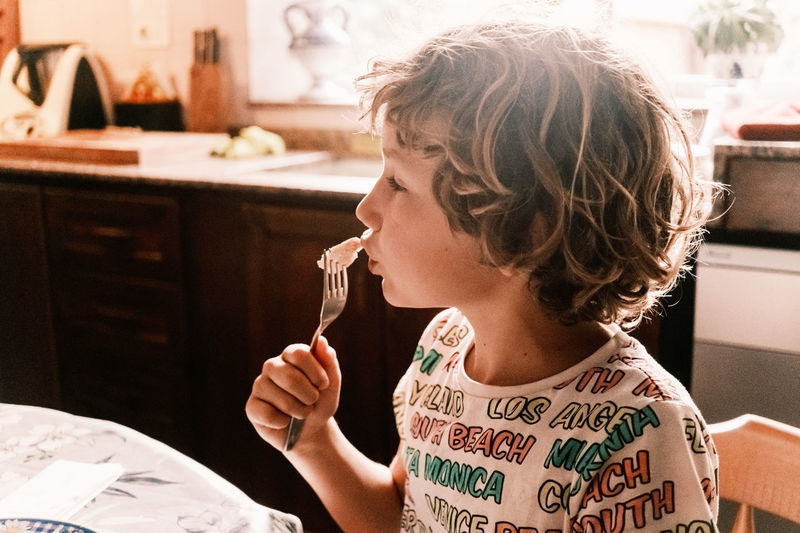 Child eats with a fork on a summer day, added film grain and out of focus background.