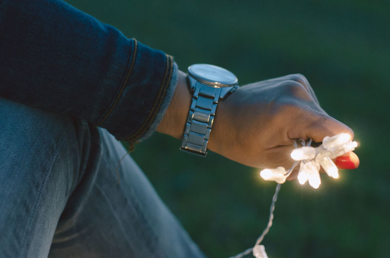 Cropped image of man holding illuminated string lights on field